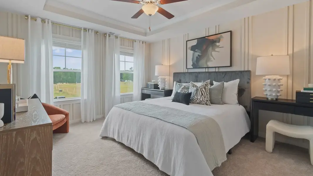 Primary Bedroom with tray ceiling, accent walls, carpet, ceiling fan, and windows