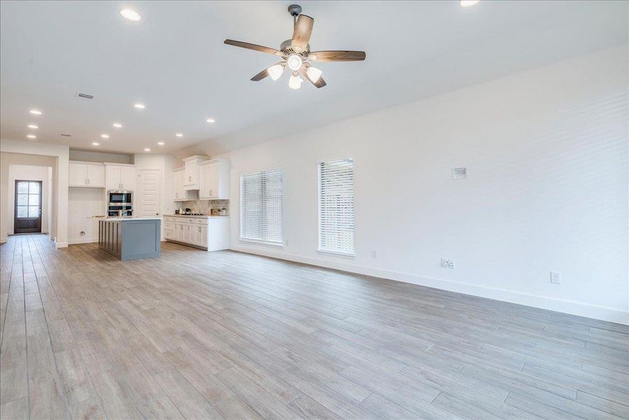 Expansive open-concept living area featuring light wood-look flooring, recessed lighting, and a ceiling fan