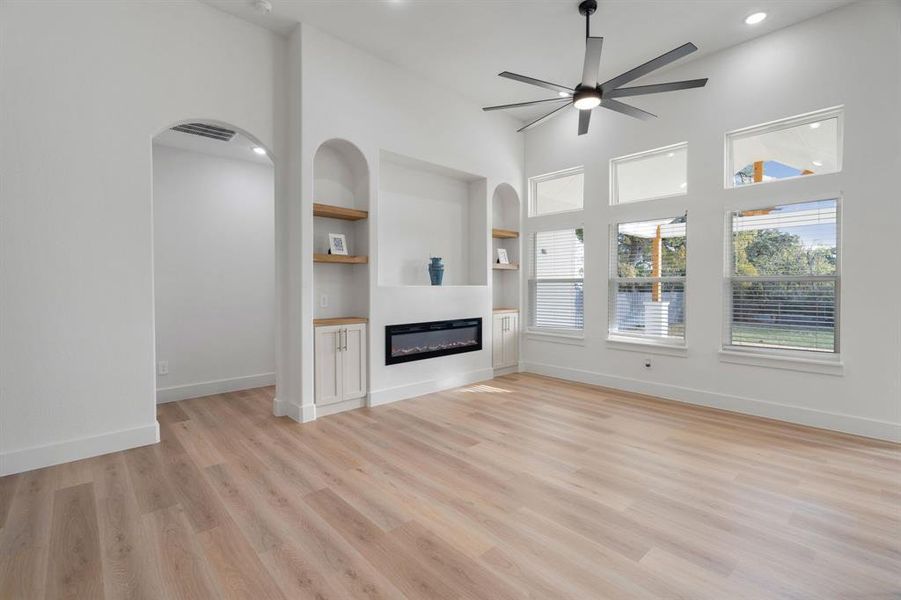 Unfurnished living room with built in shelves, ceiling fan, light wood finished floors, a glass covered fireplace, and recessed lighting