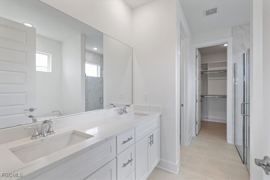 Bathroom with a spacious closet, a marble finish shower, and double vanity