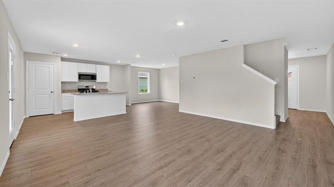Open-concept living space featuring wood-finish flooring, recessed lighting, and a kitchen with white cabinetry, stainless steel appliances, and a central island with a granite-style countertop