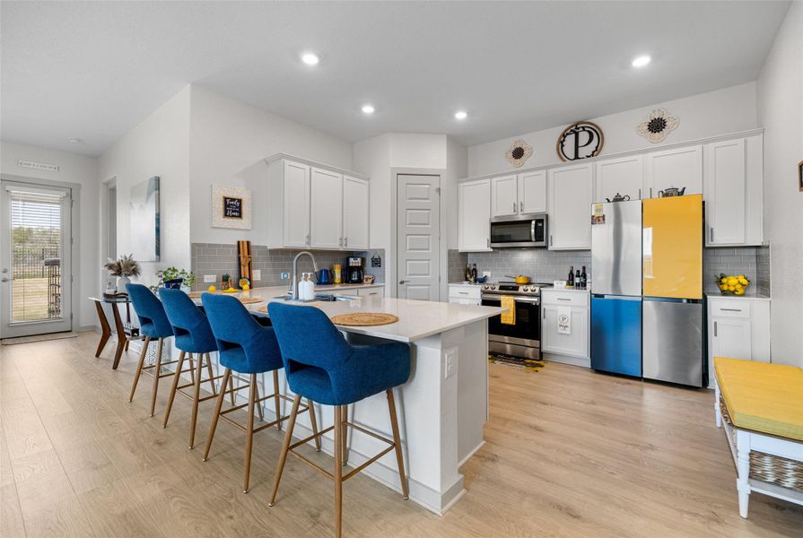 Kitchen featuring stainless steel appliances, white cabinets, a peninsula, a kitchen breakfast bar, and light wood-style flooring Kitchen featuring stainless steel appliances, white cabinets, a peninsula, a kitchen breakfast bar, and light wood-style flooring