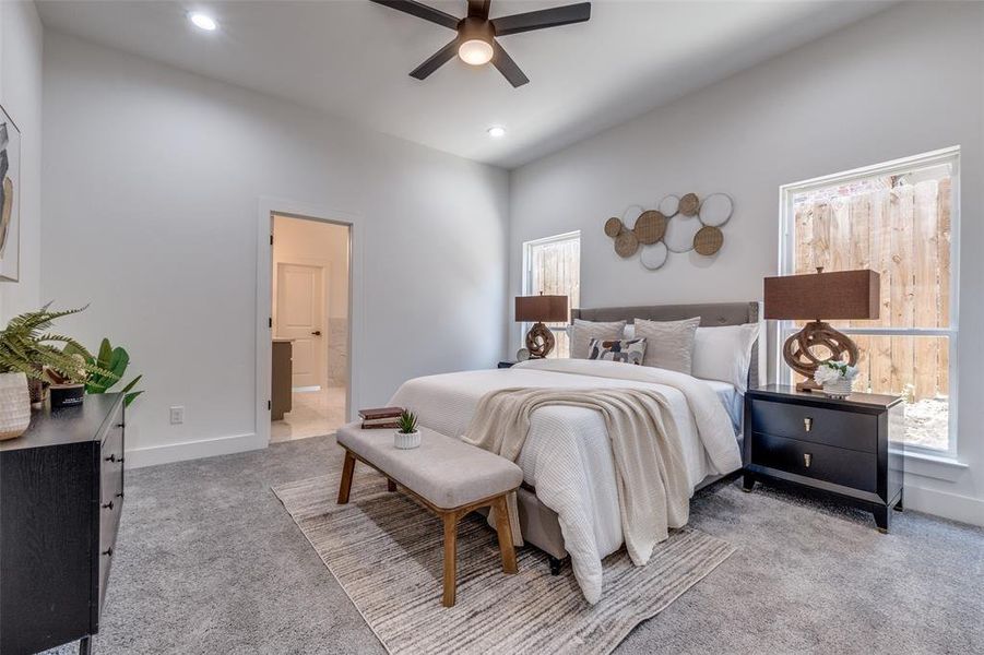 Bedroom featuring light carpet, ensuite bath, ceiling fan, and multiple windows