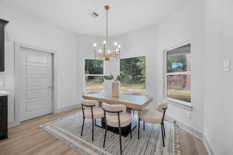 Bright dining area with large windows offering natural views. Features a modern chandelier, light wood flooring, and a stylish table set. Ideal for cozy meals and gatherings. Bright dining area with large windows offering natural views. Features a modern chandelier, light wood flooring, and a stylish table set. Ideal for cozy meals and gatherings.