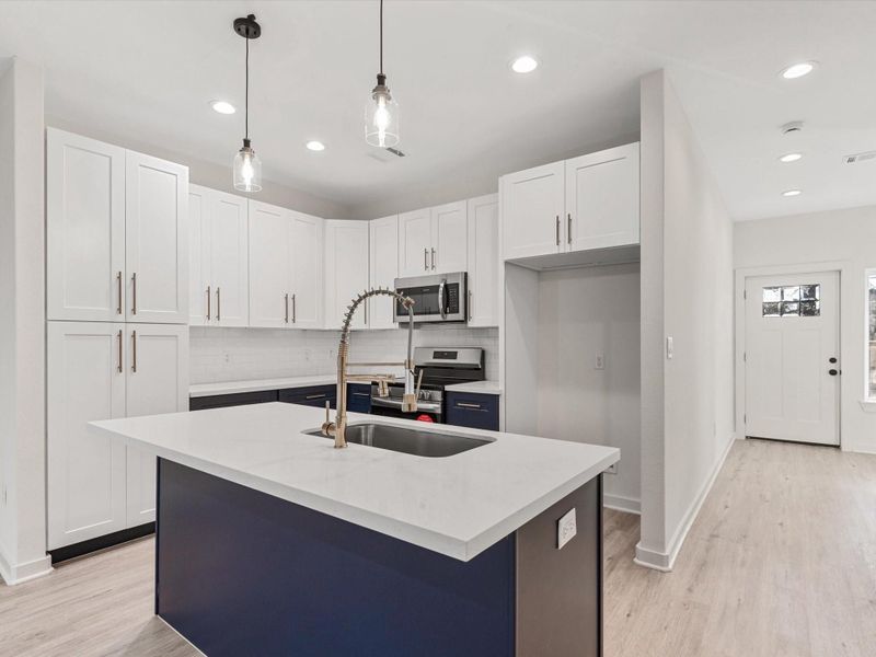 Modern kitchen with a clean design featuring white cabinetry and a dark blue island. Equipped with stainless steel appliances and a stylish faucet, it includes recessed lighting and wood flooring, creating a bright and inviting space.