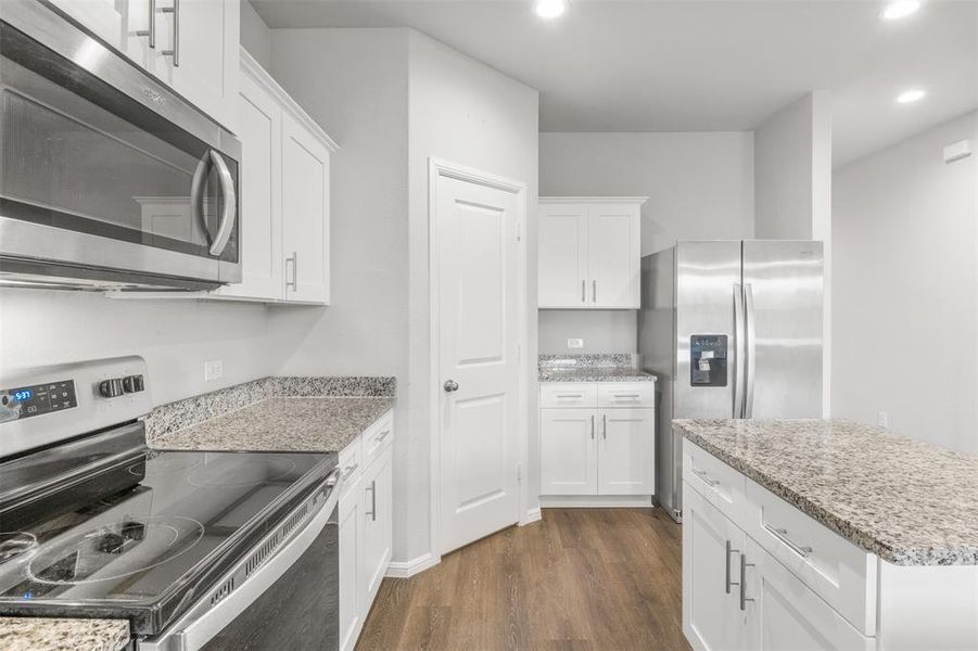 Kitchen featuring dark wood-type flooring, light stone counters, stainless steel appliances, and white cabinets