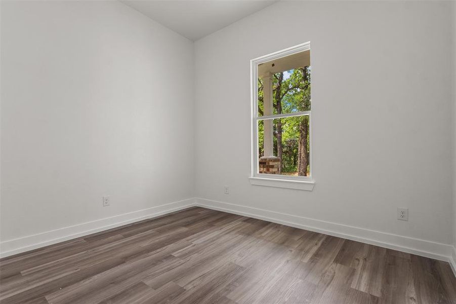 This room features light-toned walls, wood-look flooring, and a window that provides natural light and a view of trees and a partial column