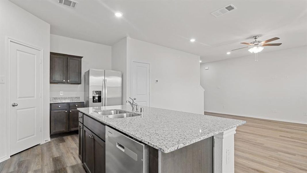 Kitchen island with a double basin stainless steel sink, a stainless steel dishwasher, and a light-toned countertop Kitchen island with a double basin stainless steel sink, a stainless steel dishwasher, and a light-toned countertop