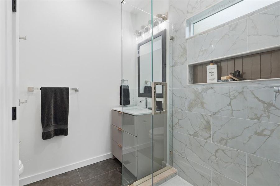 Contemporary bathroom featuring a spacious glass-enclosed shower with large format marbled tile and an integrated niche