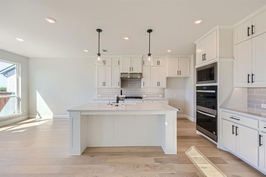 Kitchen with pendant lighting, white cabinets, and a center island with sink