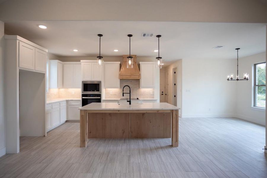 Kitchen with backsplash, white cabinetry, custom range hood, pendant lighting, and recessed lighting Kitchen with backsplash, white cabinetry, custom range hood, pendant lighting, and recessed lighting