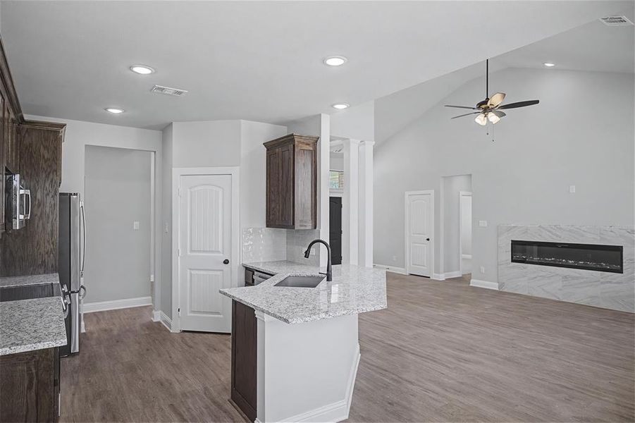 Kitchen with light stone counters, dark wood finish cabinets, a fireplace, a peninsula, and a ceiling fan