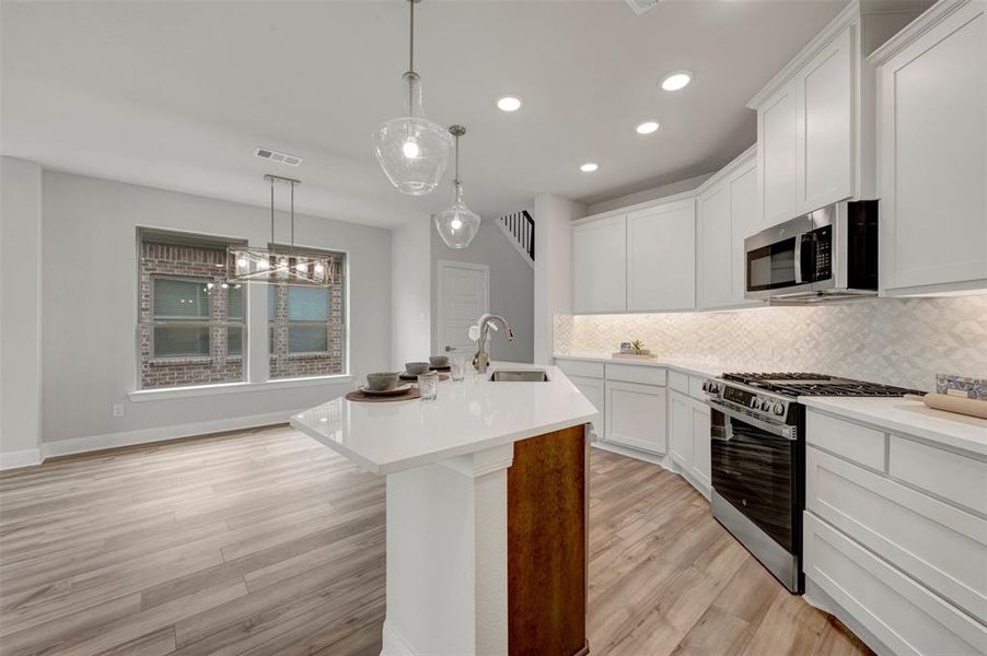 Contemporary kitchen featuring white cabinetry, stainless steel appliances, a white tile backsplash, and a central island with a sink and seating area