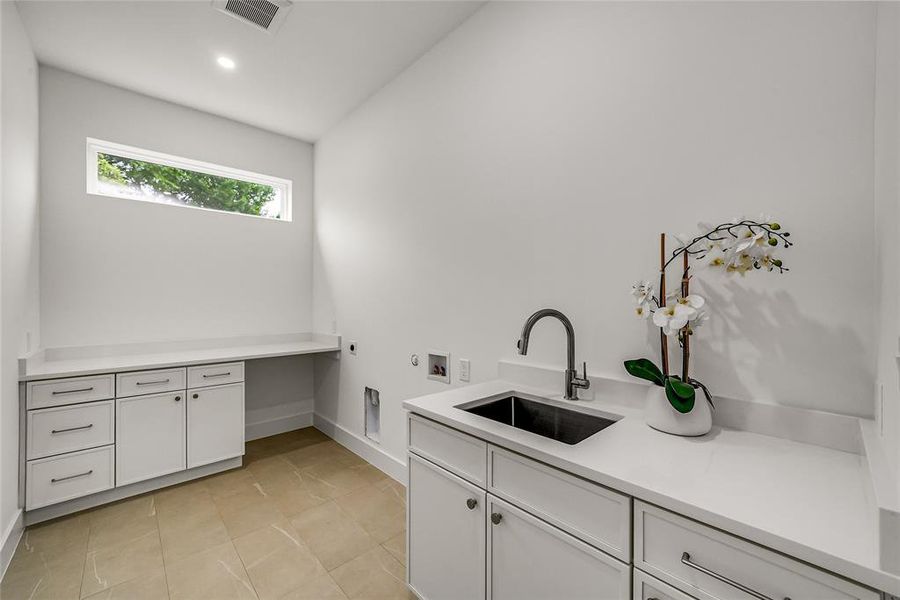 Functional utility room featuring white cabinetry, light-toned countertop surfaces, and a built-in sink with a dark faucet