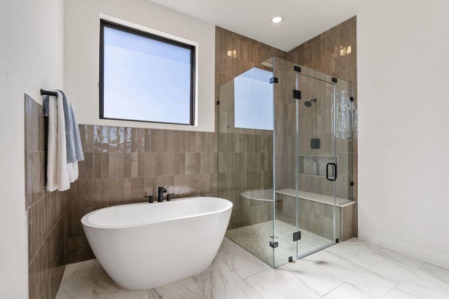 The primary bathroom showcases a sculptural freestanding soaking tub, glass enclosed walk-in shower and refined tile work throughout