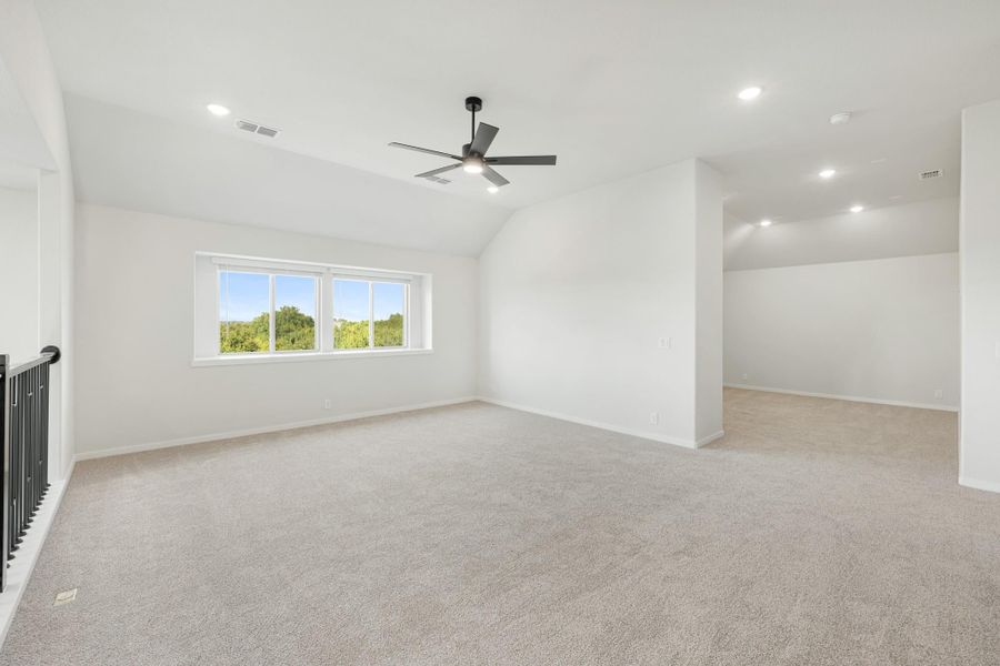 Spacious empty room with vaulted ceiling, ceiling fan, carpet flooring, and large window with tree views