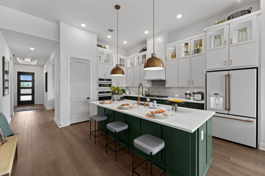 Dual tone kitchen featuring high end fridge, hanging light fixtures, dark wood-type flooring, two tone cabinets, and a breakfast bar area Dual tone kitchen featuring high end fridge, hanging light fixtures, dark wood-type flooring, two tone cabinets, and a breakfast bar area
