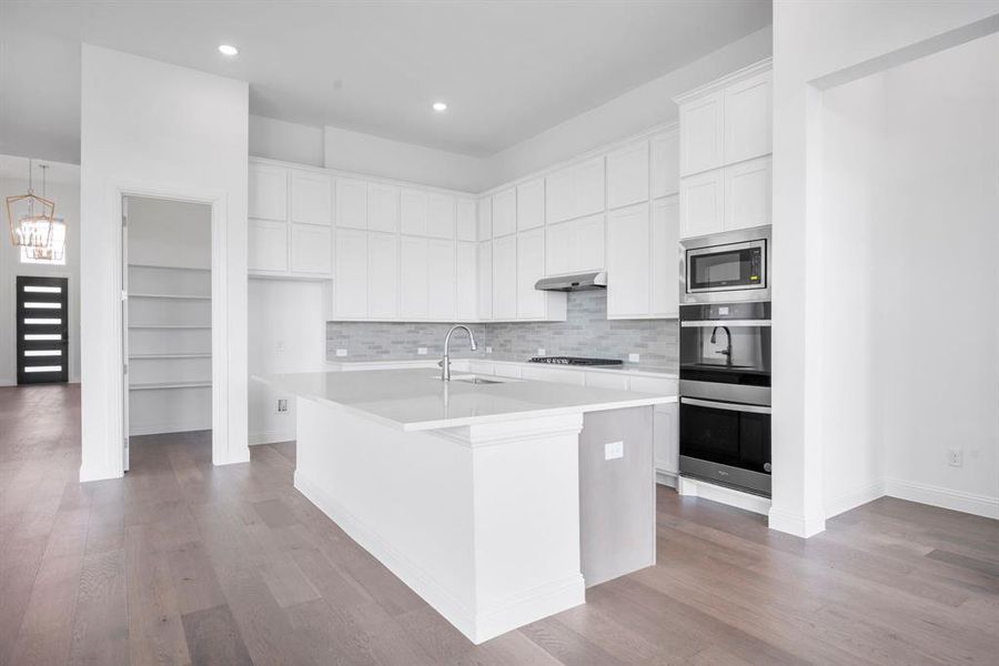 Kitchen featuring a center island with sink, backsplash, white cabinetry, light hardwood / wood-style floors, and stainless steel appliances