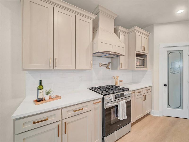 Kitchen featuring gas stove, custom range hood, tasteful backsplash, and light hardwood / wood-style floors