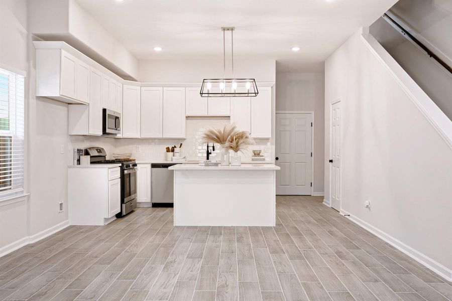 Spacious kitchen features upgraded cabinetry, crown molding, quartz countertops, stainless steel appliances, and a center island with pendant lights and bar-top seating. From a previous project with a similar floor plan