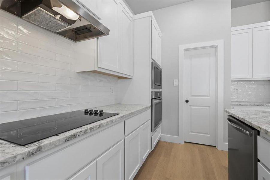 Kitchen featuring ventilation hood, backsplash, white cabinets, stainless steel appliances, and light stone counters