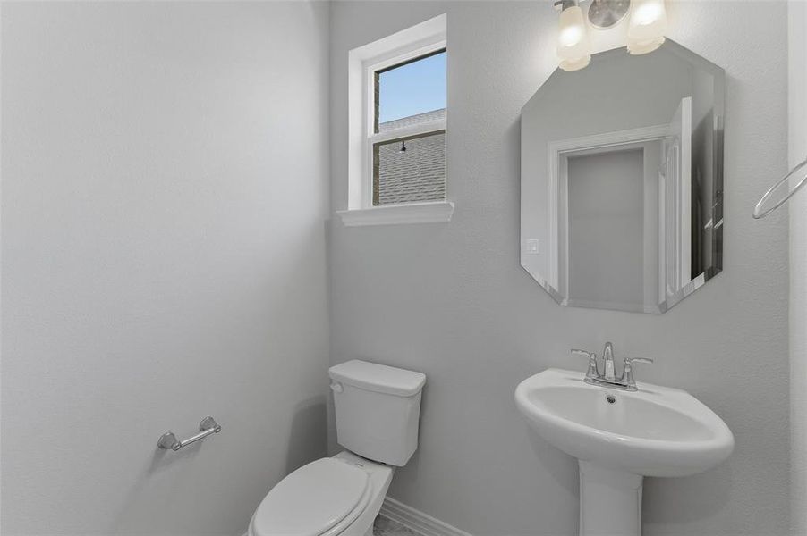 Pedestal sink with chrome faucet, complemented by an octagonal wall mirror with sconce lighting