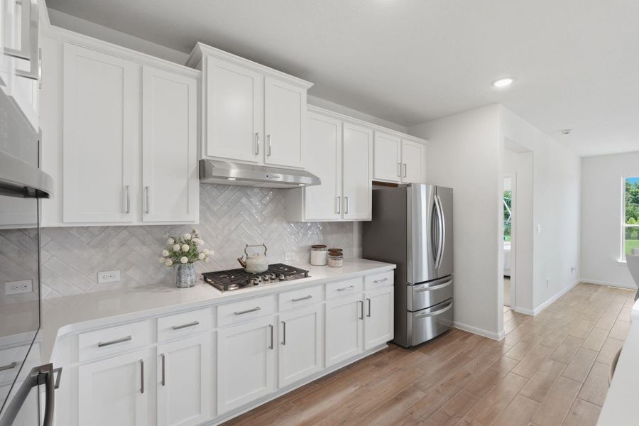 Modern kitchen with white cabinetry, stainless steel appliances, and a sleek tile backsplash. The space features a gas cooktop, ample counter space, and light wood tile flooring, creating a bright and inviting atmosphere.
