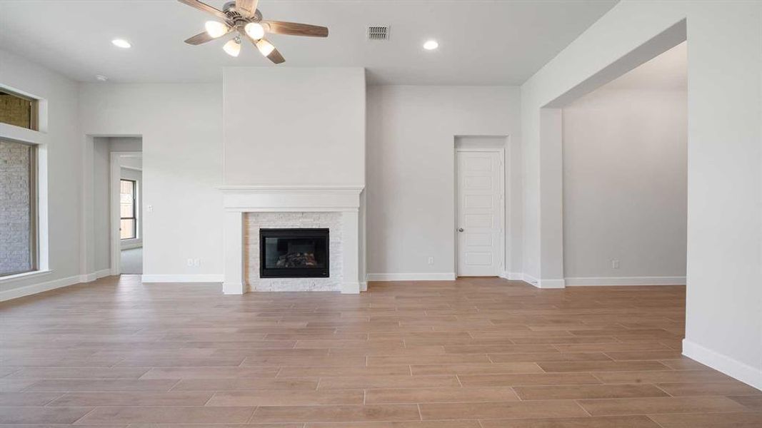 Unfurnished living room featuring ceiling fan, a stone fireplace, and light hardwood / wood-style flooring