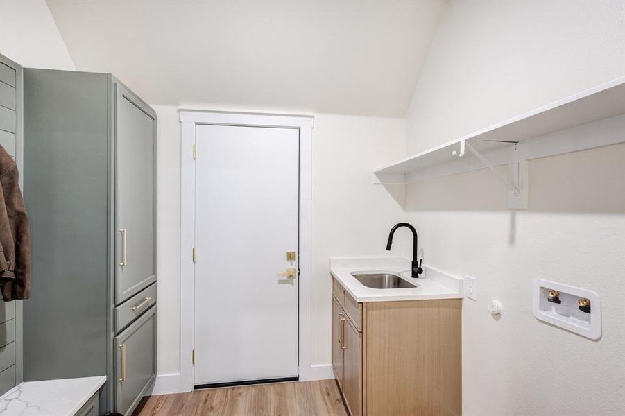 Clothes washing area featuring washer hookup, light hardwood / wood-style floors, cabinets, and sink