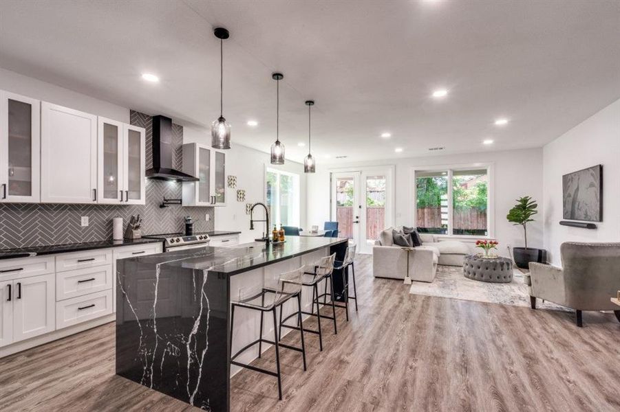 Kitchen with wall chimney exhaust hood, a kitchen bar, open floor plan, backsplash, and light wood finished floors