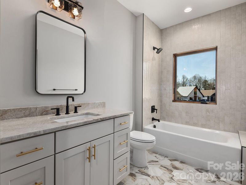 Representative photo from 50 Verde Drive showing the builder’s quality of construction and finish level, including a secondary full bath with granite countertop, Wolf cabinetry, designer mirror and lighting, ceramic tile flooring, and tiled tub/shower surround.