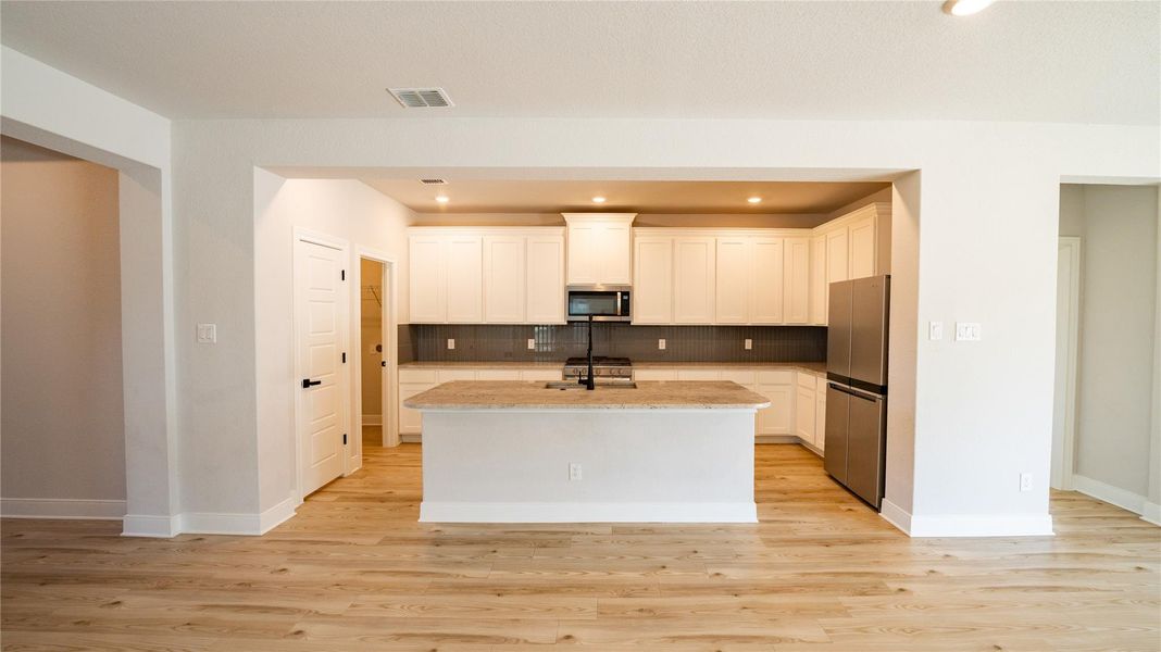 Kitchen with recessed lighting, backsplash, white cabinetry, light stone counters, and stainless steel appliances Kitchen with recessed lighting, backsplash, white cabinetry, light stone counters, and stainless steel appliances