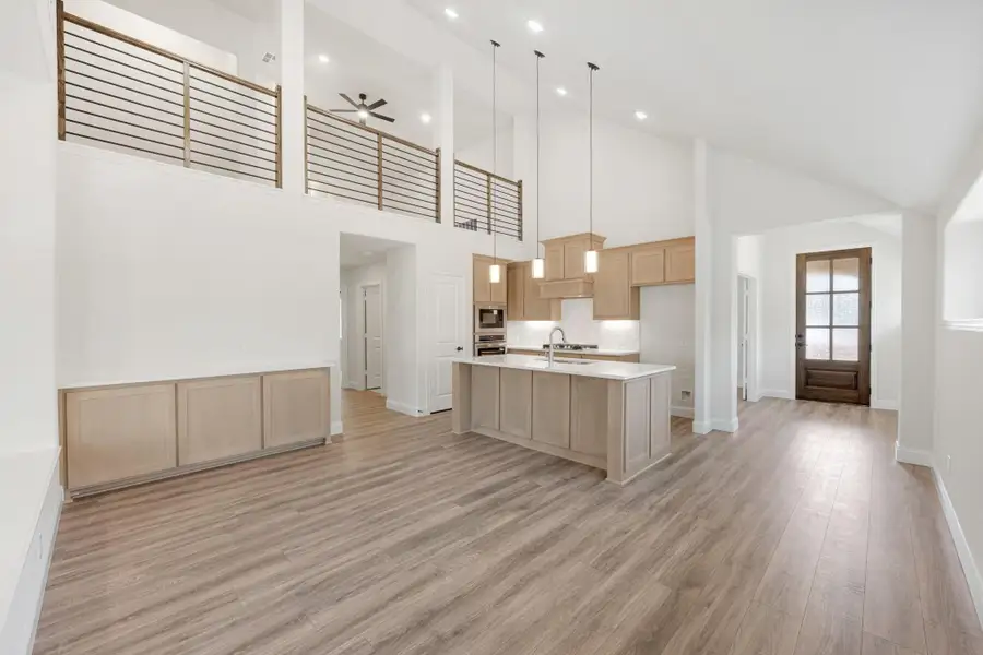 Open-concept kitchen with large island, light wood cabinets, and two-story ceiling with upper balcony railing