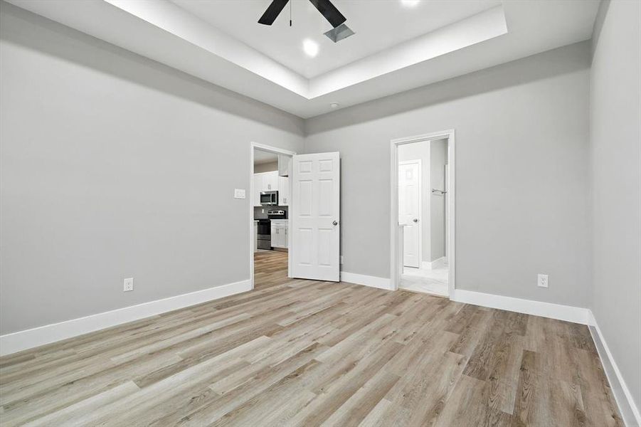 Unfurnished bedroom with light wood finished floors, a raised ceiling, ceiling fan, ensuite bath, and recessed lighting Unfurnished bedroom with light wood finished floors, a raised ceiling, ceiling fan, ensuite bath, and recessed lighting