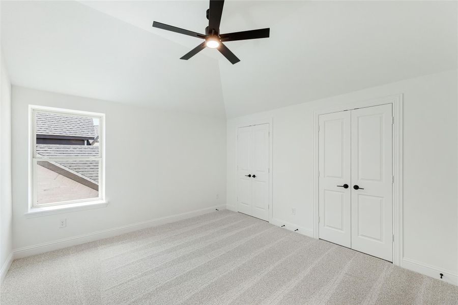 Empty bedroom with vaulted ceiling, ceiling fan, carpet floors, and two white closet doors Empty bedroom with vaulted ceiling, ceiling fan, carpet floors, and two white closet doors