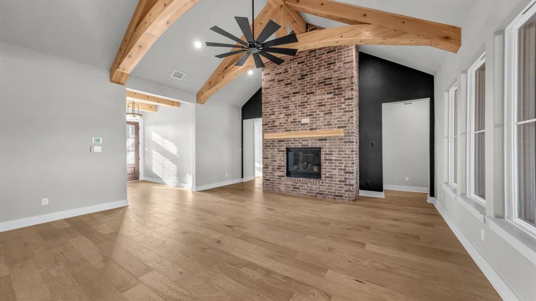 Vaulted ceiling featuring exposed wood beams, a brick-clad fireplace with a wood mantle, and wood-finish flooring Vaulted ceiling featuring exposed wood beams, a brick-clad fireplace with a wood mantle, and wood-finish flooring