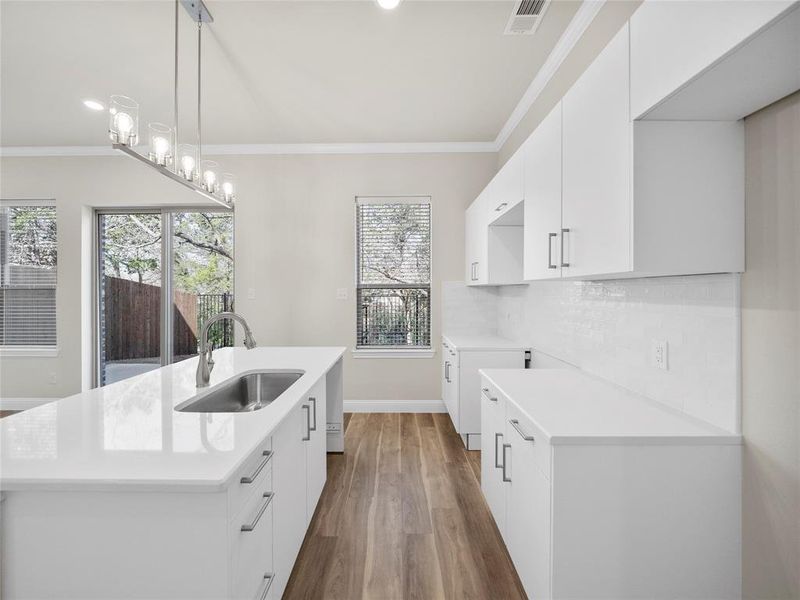 Kitchen with a sink, visible vents, light countertops, decorative backsplash, and crown molding