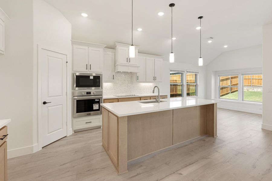 Kitchen with large center island, white cabinets, stainless steel appliances, and light wood floors
