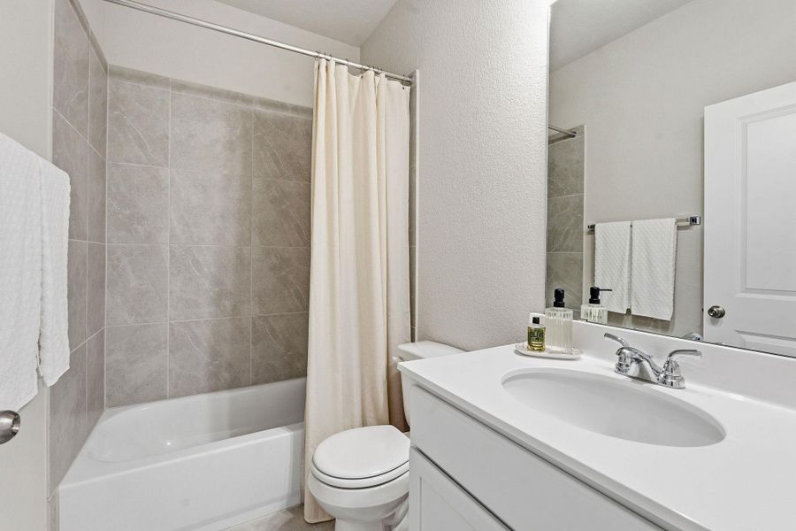 Bathroom featuring a textured wall, vanity, and shower / bath combo with shower curtain Bathroom featuring a textured wall, vanity, and shower / bath combo with shower curtain