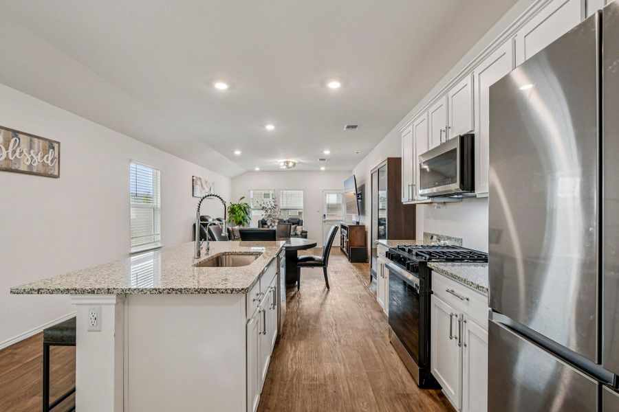 Kitchen featuring stainless steel appliances, white cabinetry, a breakfast bar, a center island with sink, and light stone countertops