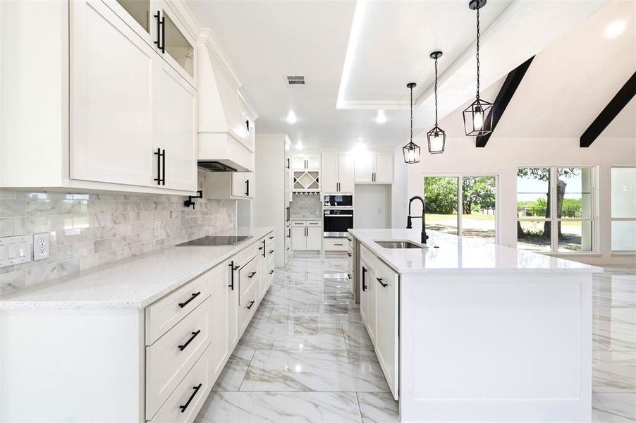 Spacious kitchen featuring an expansive island with an undermount sink, white cabinetry with matte black hardware, mosaic tile backsplash, and integrated stainless steel appliances