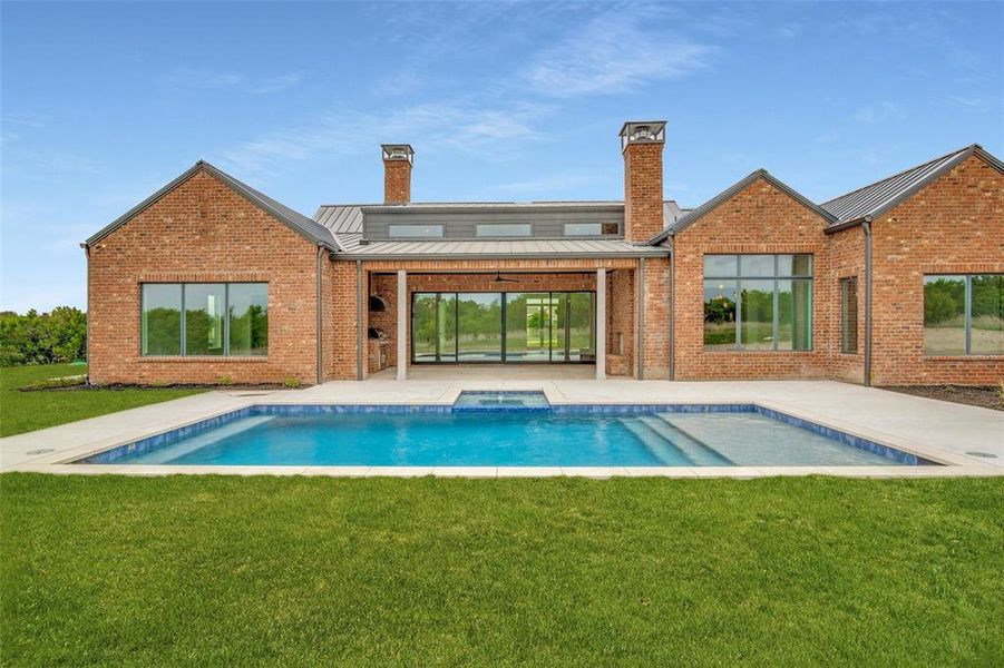 Rear view of property featuring a standing seam roof, a lawn, a chimney, and brick siding