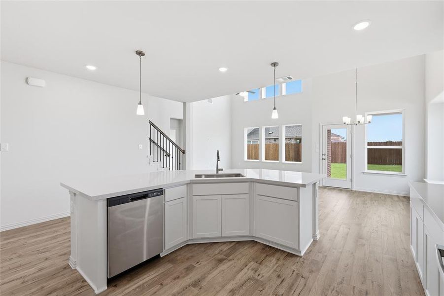 Spacious kitchen island featuring a stainless steel dishwasher, undermount sink with a gooseneck faucet, and two pendant lights