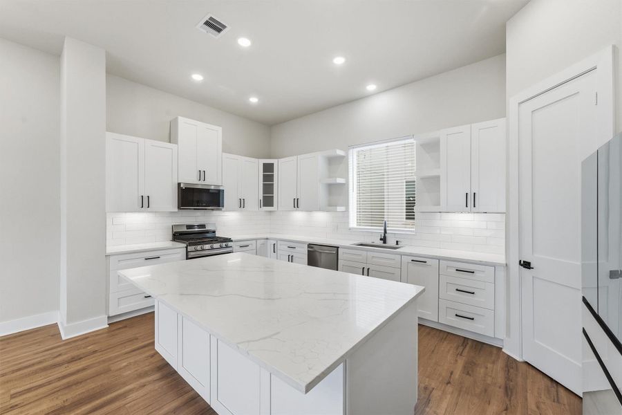 Sleek modern kitchen with a large quartz island, white shaker cabinets, stainless steel appliances, and abundant recessed lighting for a bright, open feel.