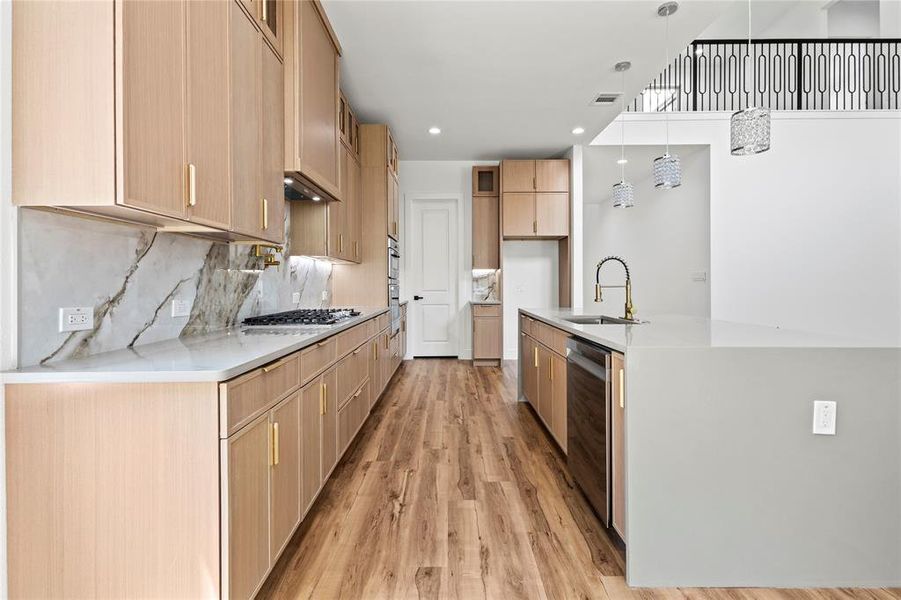 Kitchen featuring light hardwood / wood-style floors, pendant lighting, backsplash, sink, and a kitchen island with sink