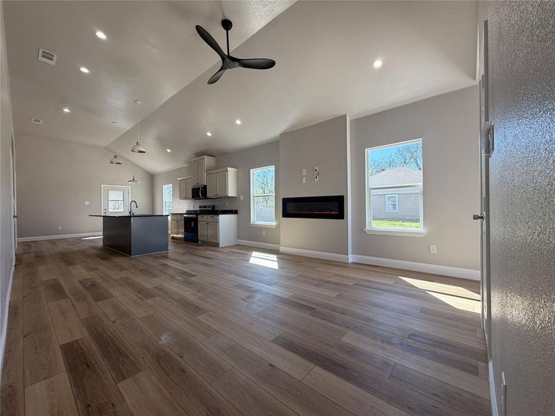 Unfurnished living room with ceiling fan, a glass covered fireplace, dark wood-style flooring, lofted ceiling, and recessed lighting