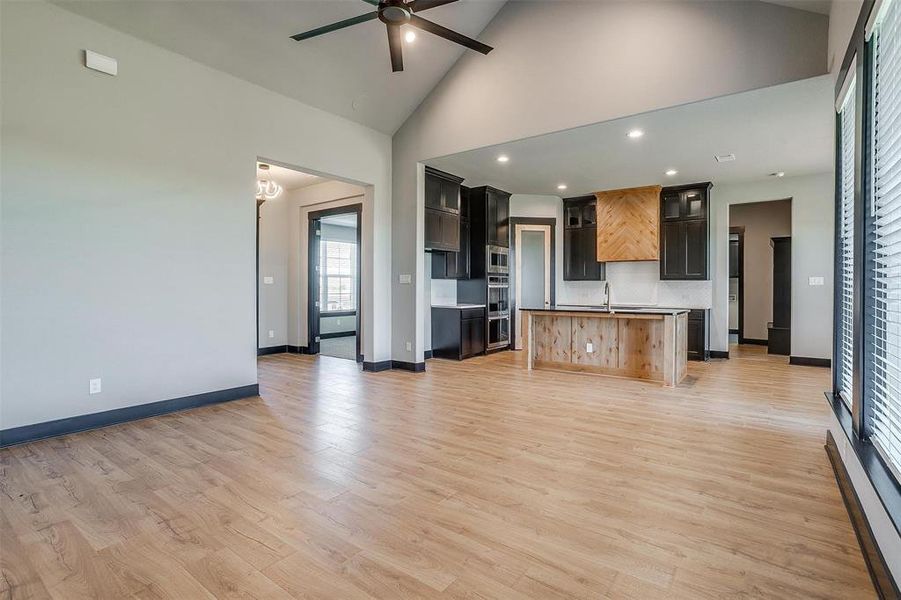 Unfurnished living room with ceiling fan, light wood-type flooring, sink, and high vaulted ceiling