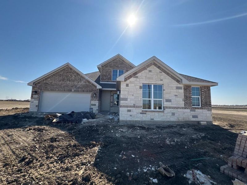 View of front facade featuring brick siding, stone siding, and an attached garage