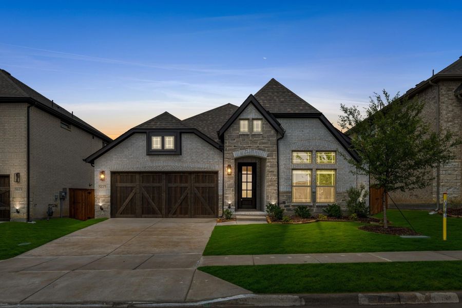 Single-story home with stone and brick exterior, two-car garage with wood doors, and manicured front lawn at dusk Single-story home with stone and brick exterior, two-car garage with wood doors, and manicured front lawn at dusk