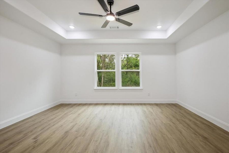 Unfurnished room with light wood finished floors, a raised ceiling, ceiling fan, and recessed lighting Unfurnished room with light wood finished floors, a raised ceiling, ceiling fan, and recessed lighting